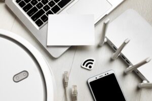 Ordinateur portable, routeur Wi-Fi, smartphone, robot aspirateur et câbles réseau posés sur une table