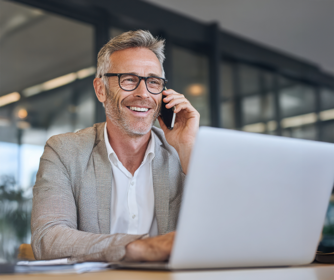 Homme souriant au téléphone devant un ordinateur portable.